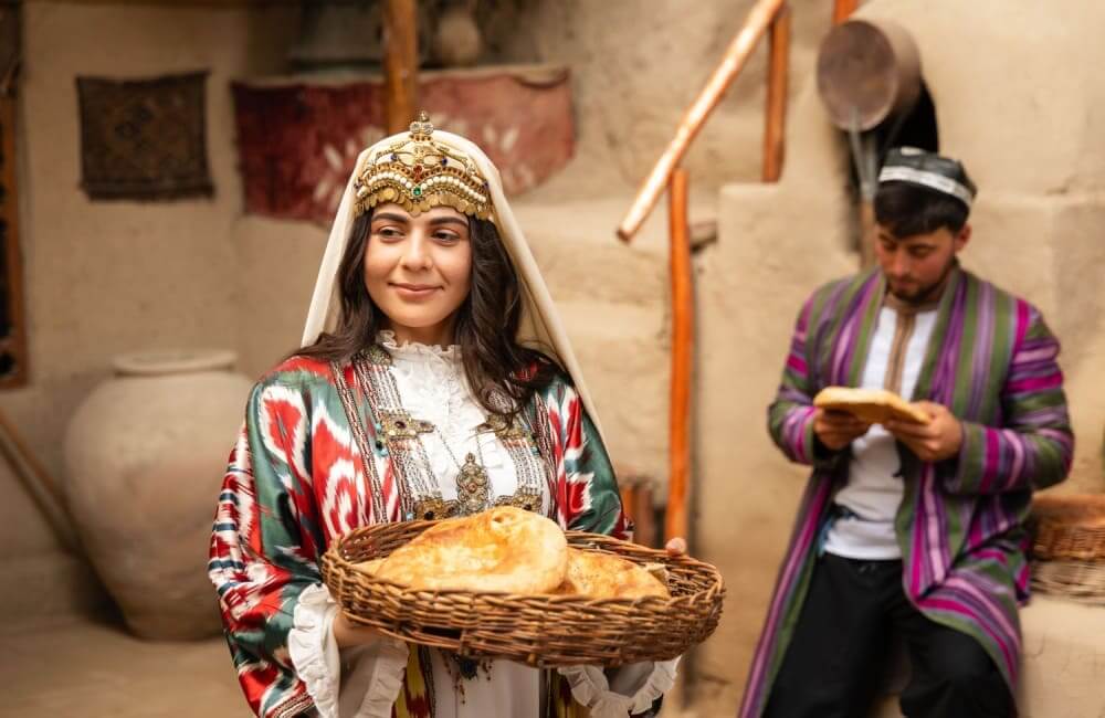 Uzbeška ženska v tradicionalni noši drži sveže pečen kruh v dvorišču
